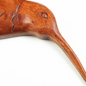 May include: A wooden carving of a bird with a long, thin beak. The bird is made of dark brown wood and has a smooth, polished finish.