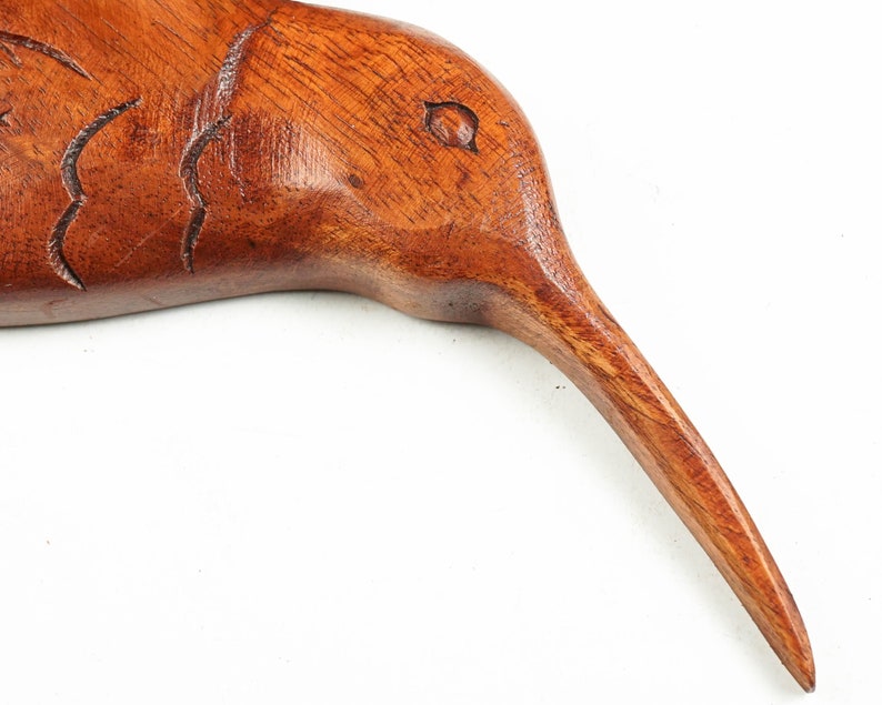 May include: A wooden carving of a bird with a long, thin beak. The bird is made of dark brown wood and has a smooth, polished finish.