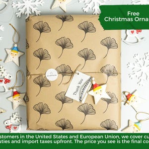 May include: A rectangular package wrapped in brown paper with a black ginkgo leaf pattern. A white circular sticker and a white rectangular tag with the text Thank You are attached with twine. The package is surrounded by various star ornaments.