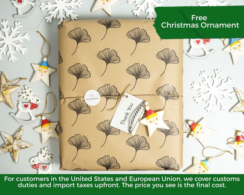 May include: A rectangular package wrapped in brown paper with a black ginkgo leaf pattern. A white circular sticker and a white rectangular tag with the text Thank You are attached with twine. The package is surrounded by various star ornaments.