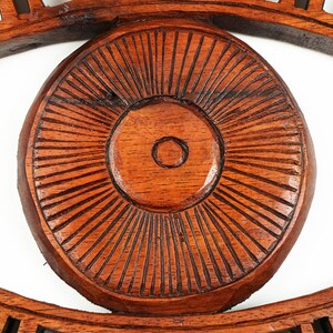 May include: A dark brown wooden wall hanging shaped like an eye. The central circular iris features a raised center surrounded by numerous thin, carved radial lines. The surrounding frame forms an almond-shaped outline with carved details.