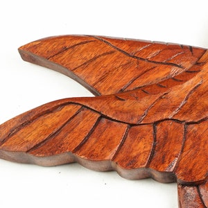 May include: A wooden carving of a bird with detailed wings. The bird is made of dark brown wood and has a natural finish.