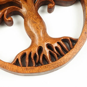 May include: A circular wooden wall hanging with a carved tree of life design. The tree has intricate branches and roots, and the wood is a rich brown color.