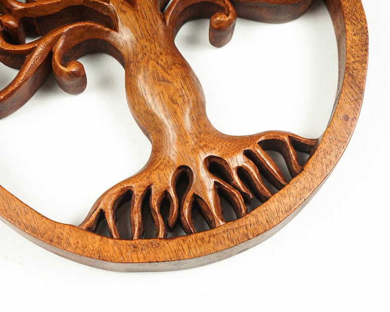 May include: A circular wooden wall hanging with a carved tree of life design. The tree has intricate branches and roots, and the wood is a rich brown color.