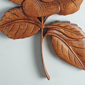 May include: A carved wooden rose with detailed leaves and a stem. The rose is a light brown color and the leaves are a darker brown.