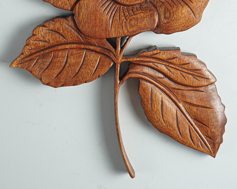 May include: A carved wooden rose with detailed leaves and a stem. The rose is a light brown color and the leaves are a darker brown.