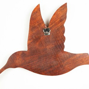May include: A wooden hummingbird wall decor with a brown stain finish. The hummingbird is in flight with its wings spread out. The decor has a metal hook on the back for hanging.