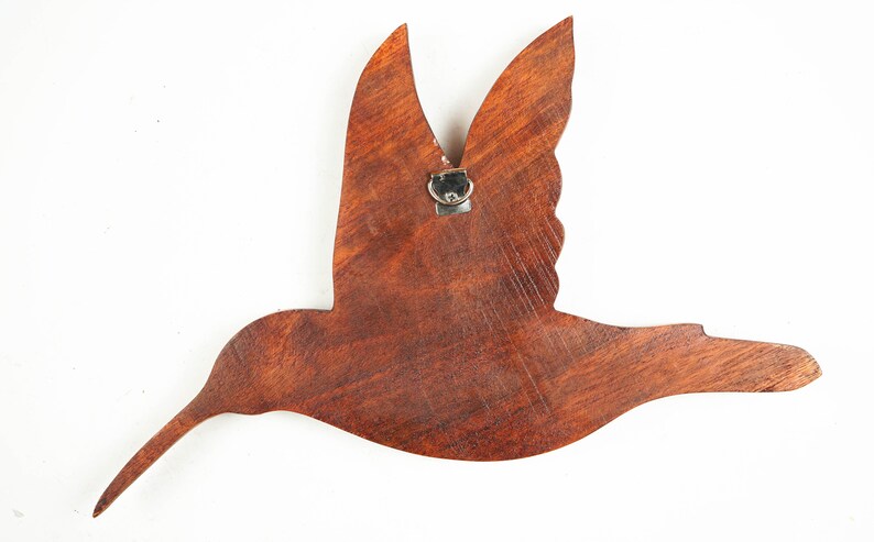 May include: A wooden hummingbird wall decor with a brown stain finish. The hummingbird is in flight with its wings spread out. The decor has a metal hook on the back for hanging.