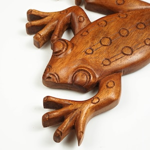 May include: A brown wooden frog carving featuring a smooth, polished finish and detailed incised circular patterns along its back and head. The sculpture displays distinct anatomical features including splayed toes and prominent eye ridges.