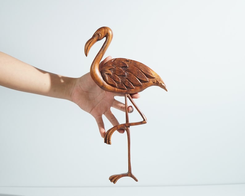 Pu&ograve; includere: Una scultura di fenicottero in legno con dettagli intricati, dipinta in un tono legno marrone. La scultura &egrave; in piedi su una sola gamba e ha le ali spiegate.