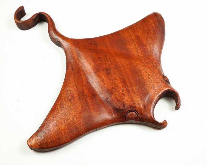 Op de afbeelding: Een handgesneden houten manta-roggen sculptuur met een roodbruine afwerking. Het beeld is gedetailleerd met realistische kenmerken en een glad, gepolijst oppervlak.