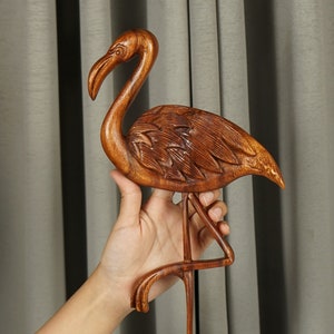 Pu&ograve; includere: Una scultura in legno di un fenicottero rosa, in piedi su una sola zampa con la testa alta. La scultura &egrave; dettagliata con le piume e ha una finitura in legno naturale.