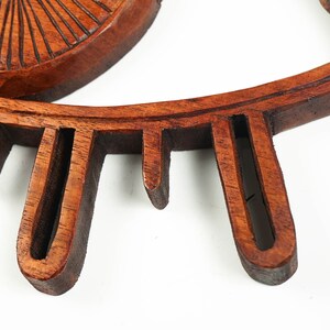 May include: A dark brown wooden wall decor piece shaped like an eye. The object features a central circular iris with carved radial lines and a surrounding almond-shaped frame with downward-pointing wooden slats representing eyelashes.