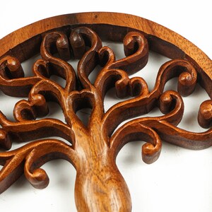 May include: A wooden wall hanging in the shape of a tree of life with intricate carvings. The tree is made of dark brown wood and has a circular shape.