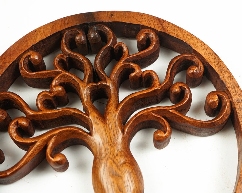 May include: A wooden wall hanging in the shape of a tree of life with intricate carvings. The tree is made of dark brown wood and has a circular shape.