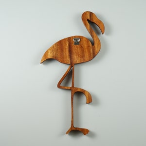 Pu&ograve; includere: Decorazione da parete in legno a forma di fenicottero con finitura in tinta marrone. Il fenicottero &egrave; in piedi su una gamba con la testa girata di lato. Il fenicottero ha un gancio di metallo sul retro per appenderlo.