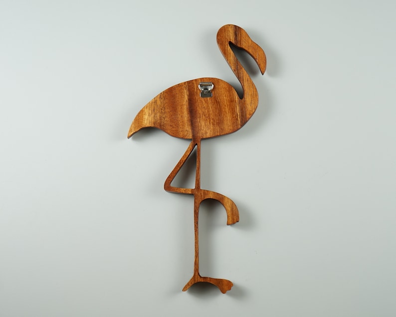Pu&ograve; includere: Decorazione da parete in legno a forma di fenicottero con finitura in tinta marrone. Il fenicottero &egrave; in piedi su una gamba con la testa girata di lato. Il fenicottero ha un gancio di metallo sul retro per appenderlo.