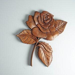 May include: A wooden carving of a rose with intricate details. The rose is carved in a light brown color and has a realistic appearance.