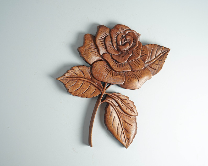 May include: A wooden carving of a rose with intricate details. The rose is carved in a light brown color and has a realistic appearance.