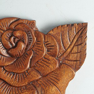 May include: A wooden carving of a rose with intricate details. The rose is carved in a dark brown wood and has a realistic appearance.