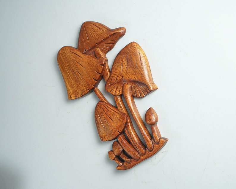 Op de afbeelding: Een handgesneden houten wanddecoratie met een groep van vijf paddenstoelen van verschillende groottes. Het beeldhouwwerk toont een rijke bruine houtnerf met gedetailleerde verticale lijnen in de hoeden en stelen van de paddenstoelen.