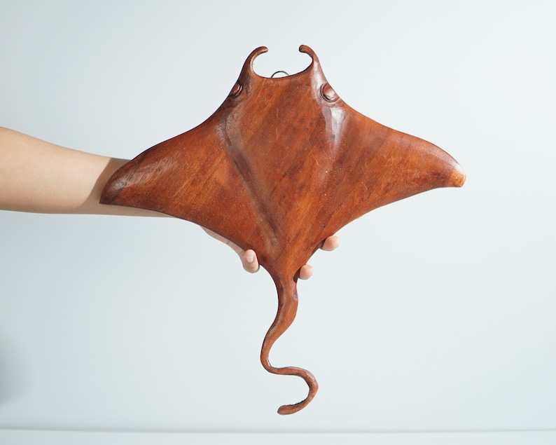Op de afbeelding: Een houten sculptuur van een mantarog, geschilderd in een rijke bruine kleur. Het beeld is gedetailleerd met realistische kenmerken, waaronder de vinnen en de staart van de mantarog.