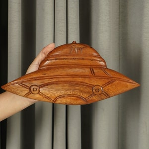 Peut inclure: Une sculpture en bois d'une soucoupe volante, avec des d&eacute;tails complexes et une finition en bois brun.