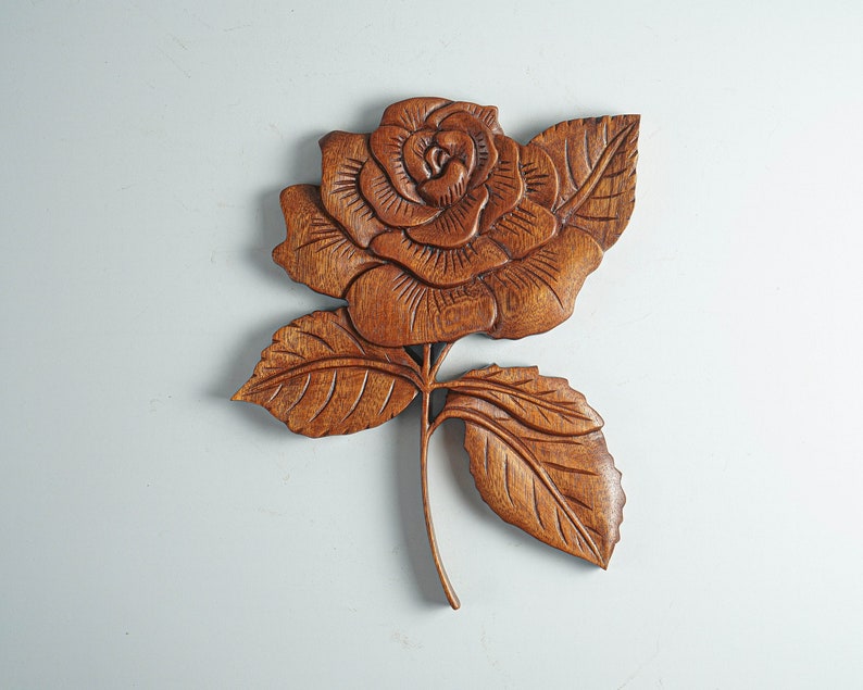May include: A wooden carving of a rose with intricate details. The rose is brown and has a natural wood finish. The carving is a beautiful example of traditional craftsmanship.