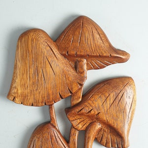Op de afbeelding: Een wanddecoratie bestaande uit een groep van drie uit hout gesneden paddenstoelen met zichtbare houtnerven. Het bruine houten beeldhouwwerk vertoont gedetailleerde verticale groeven op de hoeden en stelen voor een textuur.