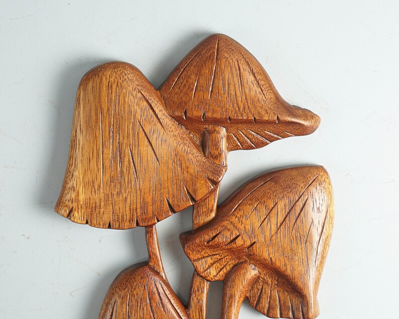 Op de afbeelding: Een wanddecoratie bestaande uit een groep van drie uit hout gesneden paddenstoelen met zichtbare houtnerven. Het bruine houten beeldhouwwerk vertoont gedetailleerde verticale groeven op de hoeden en stelen voor een textuur.
