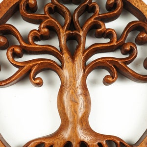 May include: A brown wooden tree of life wall decor with intricate carvings. The tree is surrounded by a circular frame.