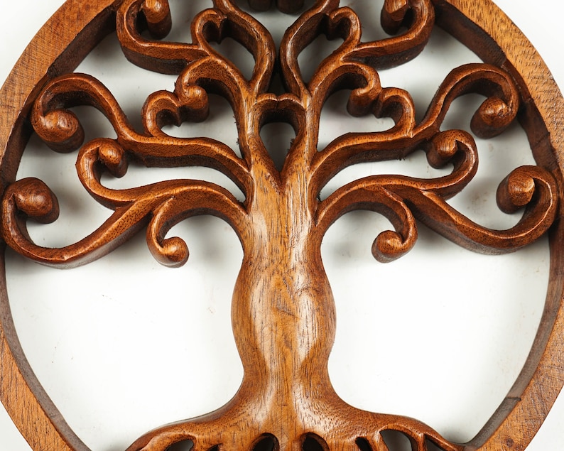 May include: A brown wooden tree of life wall decor with intricate carvings. The tree is surrounded by a circular frame.
