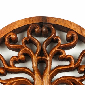 May include: A circular wooden wall decor with a carved tree of life design. The intricate details of the branches and leaves are highlighted by the rich brown color of the wood.