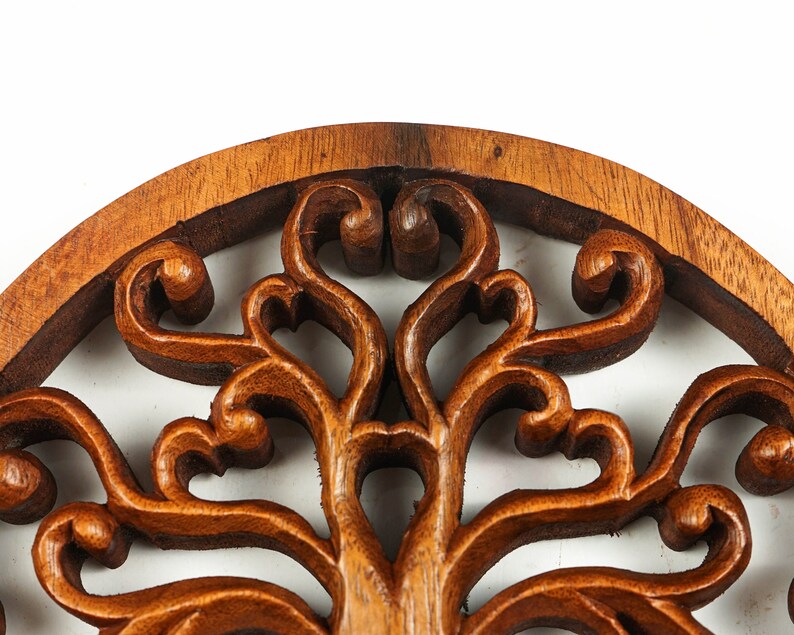 May include: A circular wooden wall decor with a carved tree of life design. The intricate details of the branches and leaves are highlighted by the rich brown color of the wood.