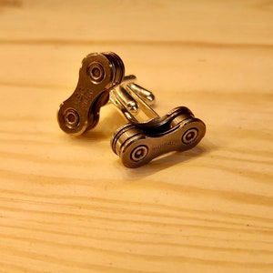 May include: A pair of silver cufflinks made from a bicycle chain link. The cufflinks are engraved with the word "SHIMANO".