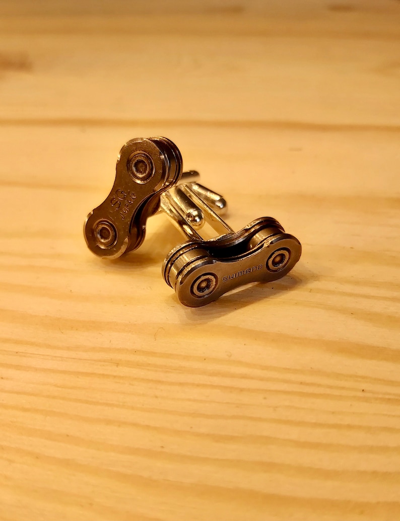 May include: A pair of silver cufflinks made from a bicycle chain link. The cufflinks are engraved with the word "SHIMANO".