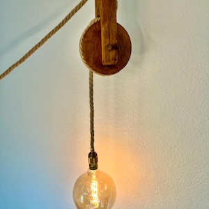May include: A wooden pulley with a rope hanging from it. A light bulb is attached to the end of the rope.