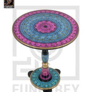 May include: A round, wooden side table with a colorful, intricate design. The table top is painted in shades of pink, blue, and gold, with a mandala-like pattern. The base of the table is also painted with a similar design, and it has four legs.