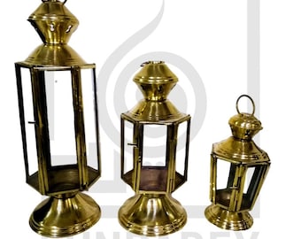 May include: Three gold metal lanterns of varying sizes with glass panels. The lanterns have a traditional design with a domed top and a square base.