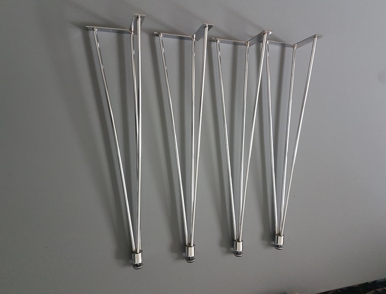 May include: Set of five silver hairpin table legs. Each leg has a flat mounting plate and tapers to a pointed end. The legs are made of shiny metal and are arranged against a gray background. These legs are designed for furniture construction.