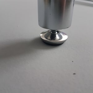 May include: Close-up of a shiny, chrome-colored furniture leg with a rounded base and a black rubber pad. The leg is attached to a metal base, and the image is taken from a low angle.