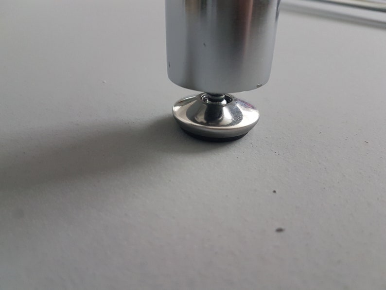 May include: Close-up of a shiny, chrome-colored furniture leg with a rounded base and a black rubber pad. The leg is attached to a metal base, and the image is taken from a low angle.