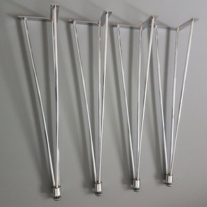 May include: Set of four silver hairpin table legs. Each leg features a flat mounting plate and tapers to a rounded tip. The legs are made of shiny metal and are displayed against a gray background.