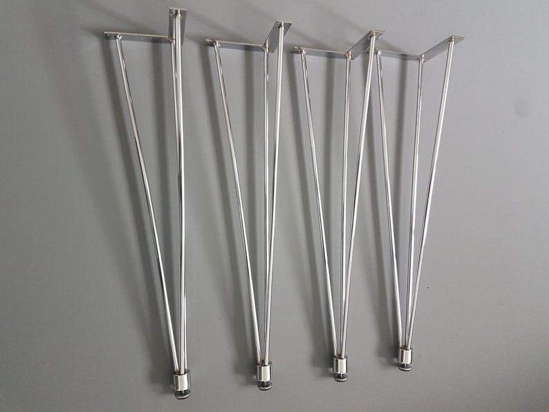 May include: Set of four silver hairpin table legs. Each leg features a flat mounting plate and tapers to a rounded tip. The legs are made of shiny metal and are displayed against a gray background.