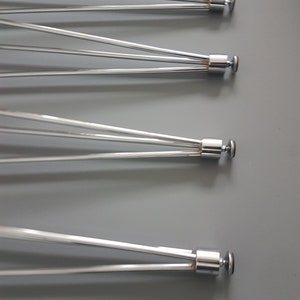May include: Four stainless steel bicycle wheel spokes, each with multiple thin, silver rods radiating from a central hub. The spokes are arranged diagonally against a gray background, showcasing their design and construction.