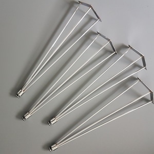May include: A collection of silver-colored metal table legs. Each leg has a triangular top and three slender, angled supports. The legs are designed for furniture construction and are displayed against a gray background.