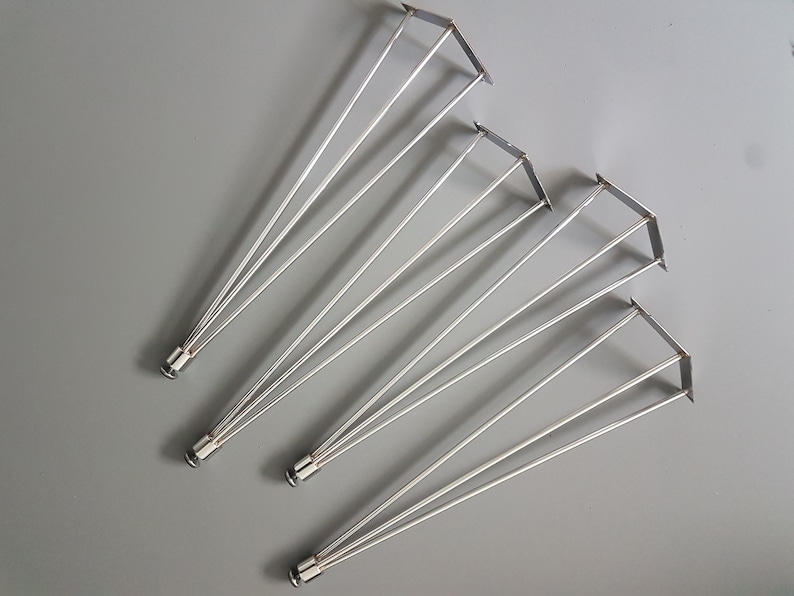 May include: A collection of silver-colored metal table legs. Each leg has a triangular top and three slender, angled supports. The legs are designed for furniture construction and are displayed against a gray background.