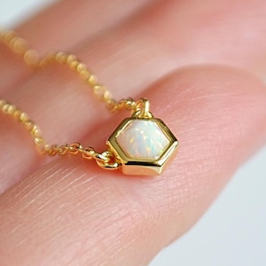 May include: A delicate gold chain necklace with a small hexagonal pendant featuring a white opal gemstone.