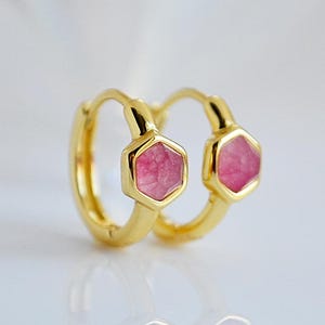 Op de afbeelding: Een paar gouden creolen met roze zeshoekige edelstenen. De oorbellen zijn klein en delicaat.
