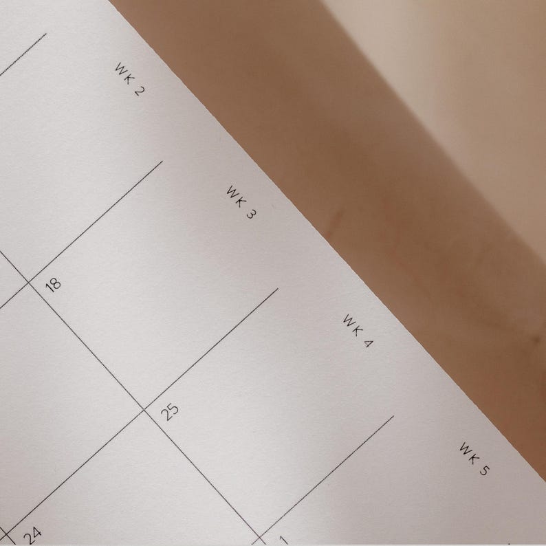 K&ouml;nnte beinhalten: Nahaufnahme eines wei&szlig;en Papierkalenders mit schwarzen Rasterlinien. Der Kalender zeigt die Wochen mit den Bezeichnungen WK 2, WK 3, WK 4 und WK 5. Die Daten 18, 24, 25 und 1 sind sichtbar.